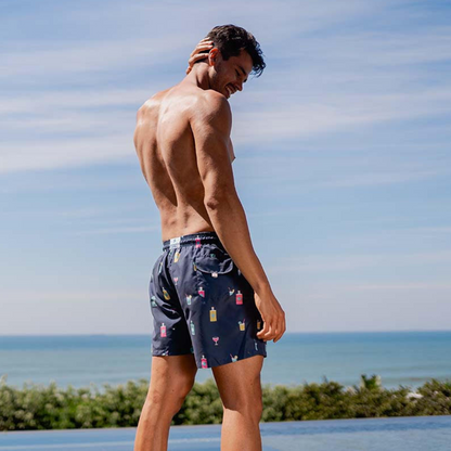 Breazies - Gin Party: men's swimming shorts. navy blue with colourful gin bottles and glasses. Quick drying, with a mid length cut. Elastic waistband, draw string with branded tips
